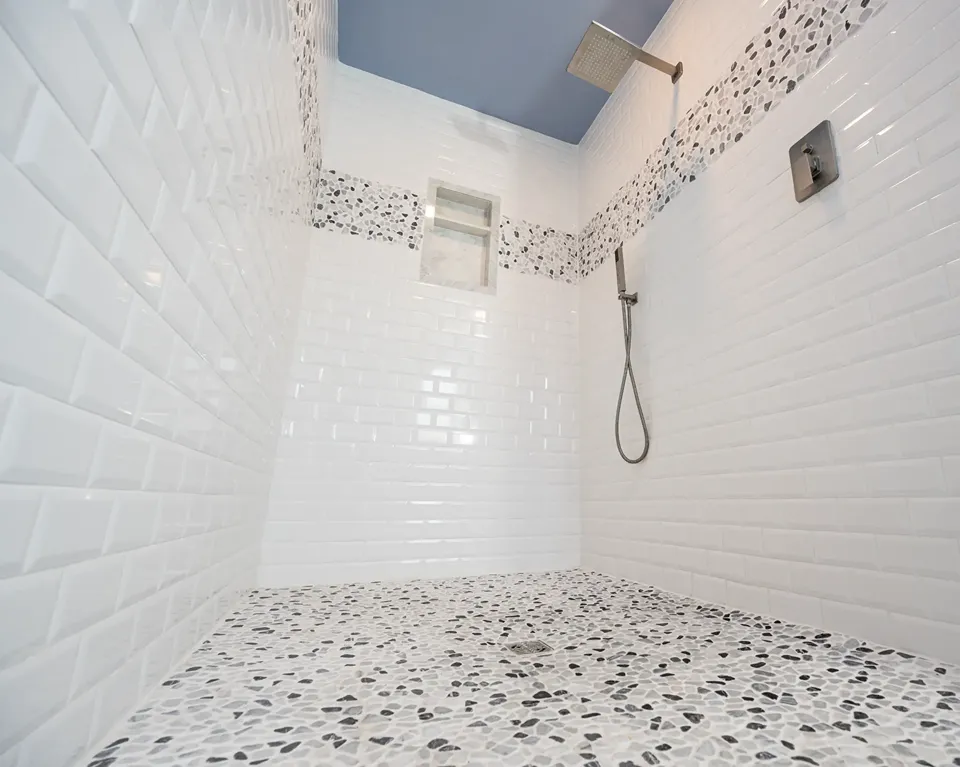 Natural pebble mosaic shower floor pitched in a single plane to a stainless linear drain set against Calacatta marble look large format shower wall tile in a Tampa FL bathroom remodel by CMK Construction