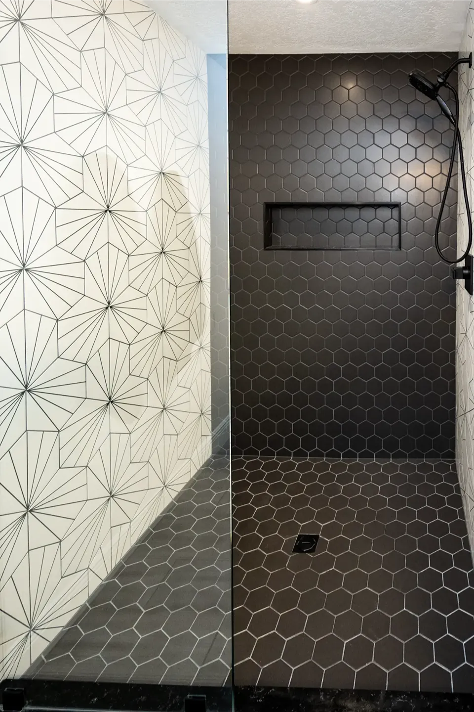 Matte black hexagon tile covering the shower walls and floor with a black recessed linear niche beside a white starburst patterned hexagon feature wall in a Tampa FL bathroom remodel by CMK Construction