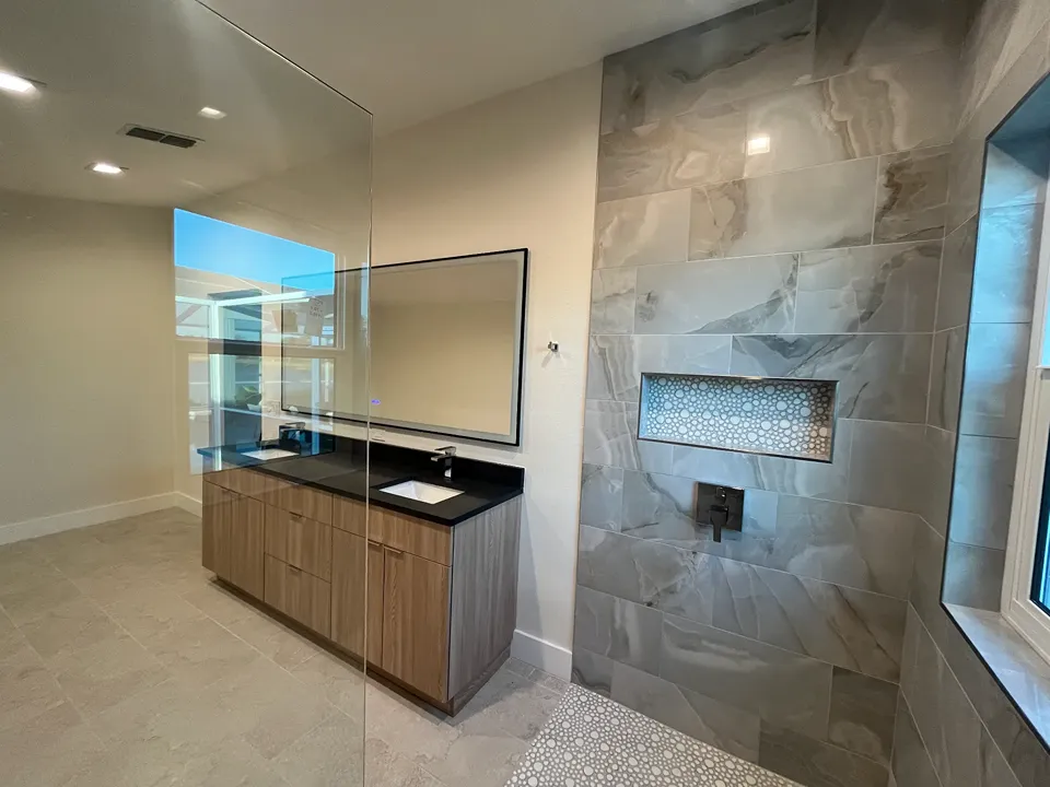 Curbless walk in shower with polished gray onyx look large format wall tile, a wide recessed niche lined in white penny round mosaic with metal edge trim, and a penny round mosaic floor beside a floating wood look vanity in a Tampa FL bathroom remodel by CMK Construction