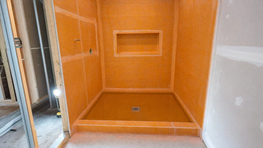 Shower covered in orange waterproofing membrane with a niche and drain, flood tested with standing water before tile