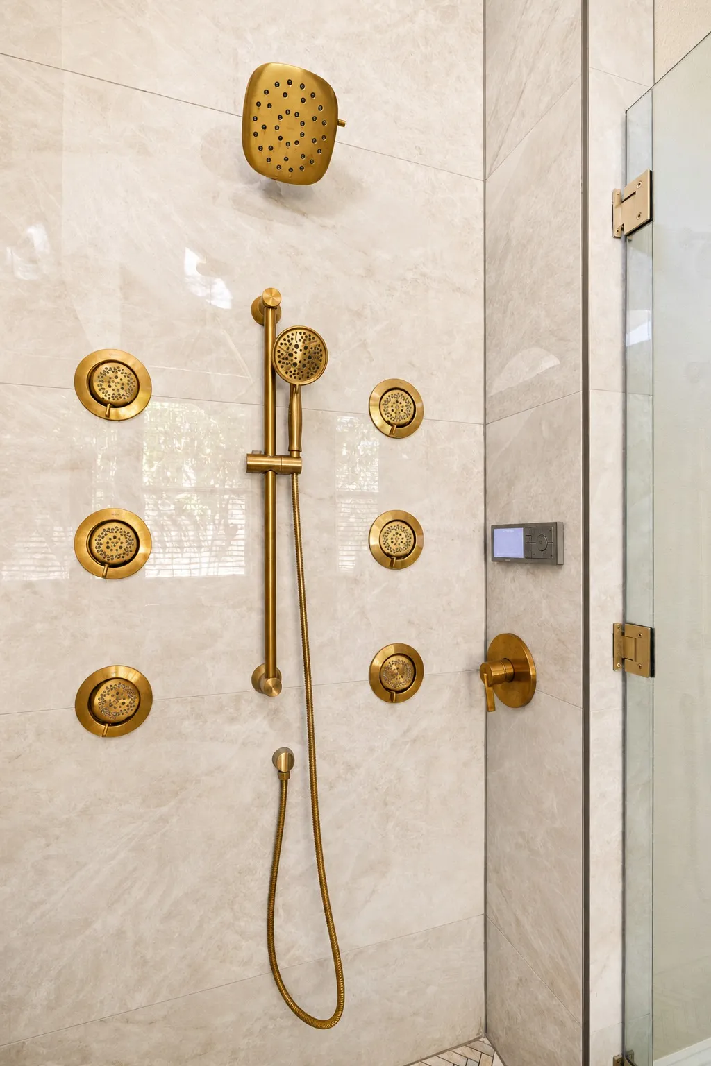 Spa shower system with champagne gold rain showerhead, six body sprays, handheld wand, and digital controls on large-format porcelain tile in Trinity, Florida by CMK Construction