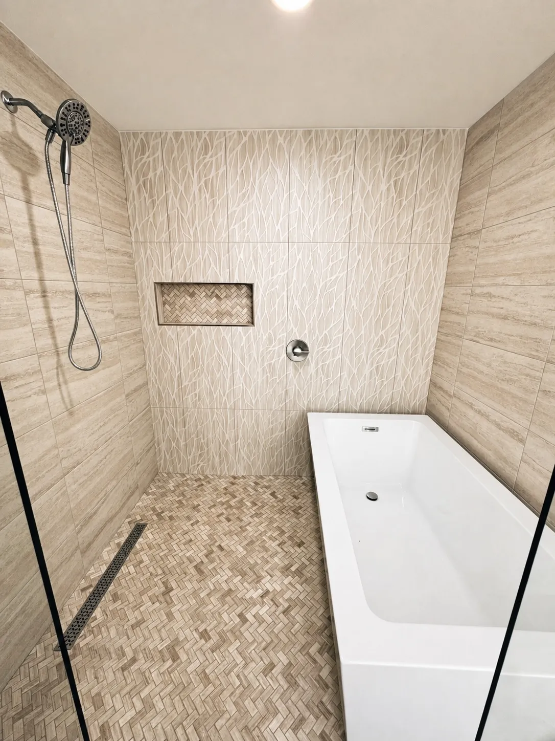 Spa style wet room with soaking tub, herringbone mosaic floor tile, decorative accent wall, linear drain, and frameless glass in Lutz, Florida by CMK Construction