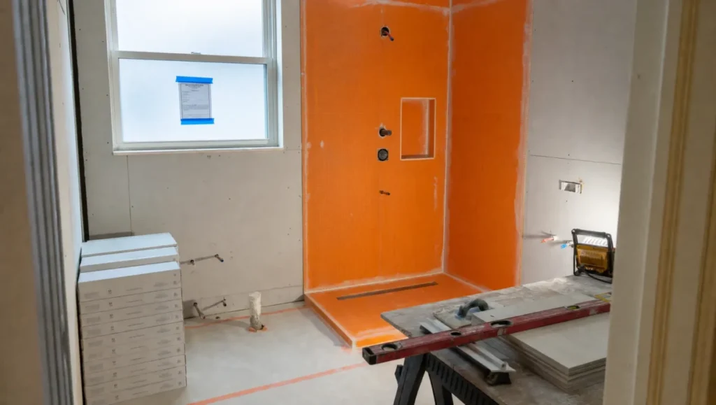 Tampa Bay bathroom renovation in progress with orange waterproofing membrane in the shower and a permit posted for inspection
