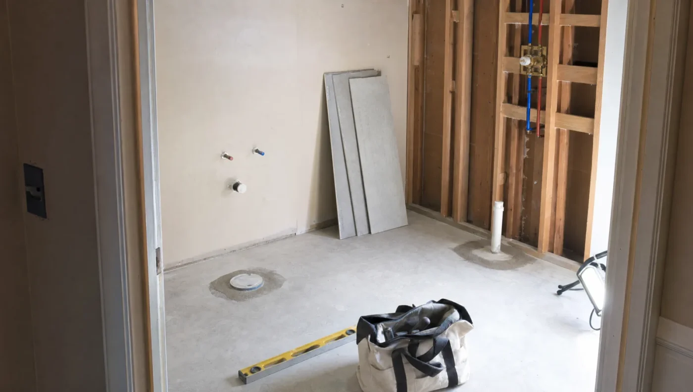 Master bathroom during a full gut remodel in a Florida slab-on-grade home, with the shower wall opened to the studs, new PEX lines and a shower valve, a capped toilet flange and cement board ready to install