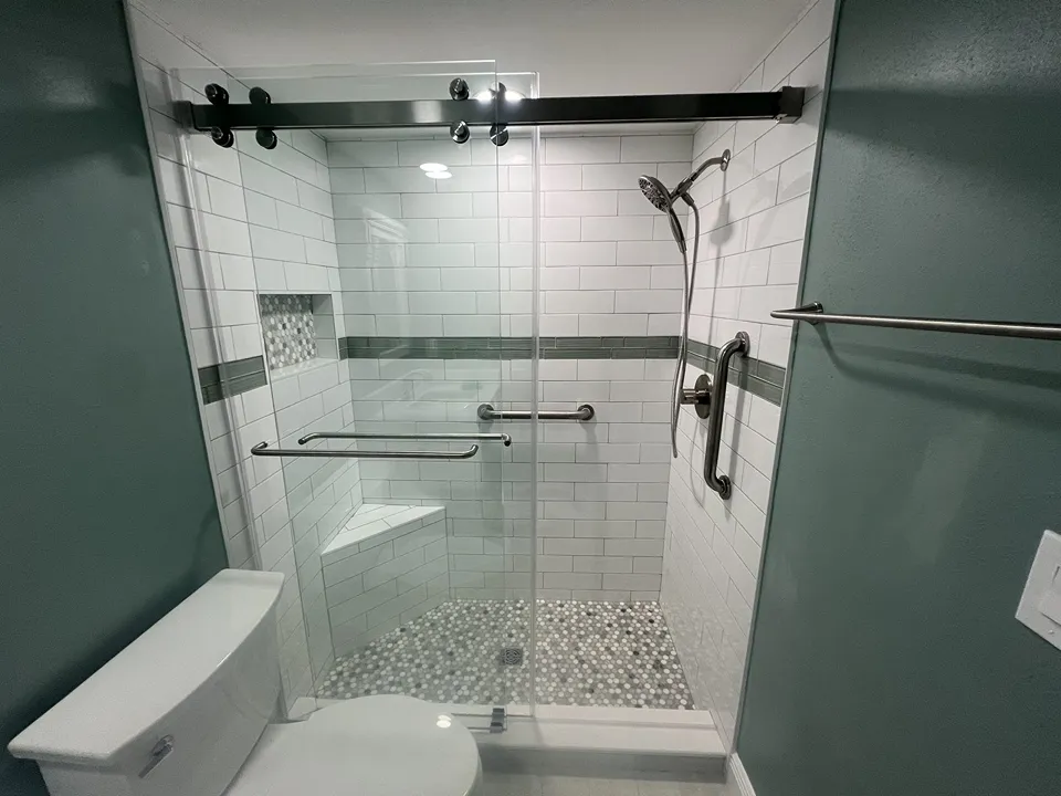 Corner bench in a tub to shower conversion with white subway tile, green glass accent band, and penny round mosaic floor on Siesta Key