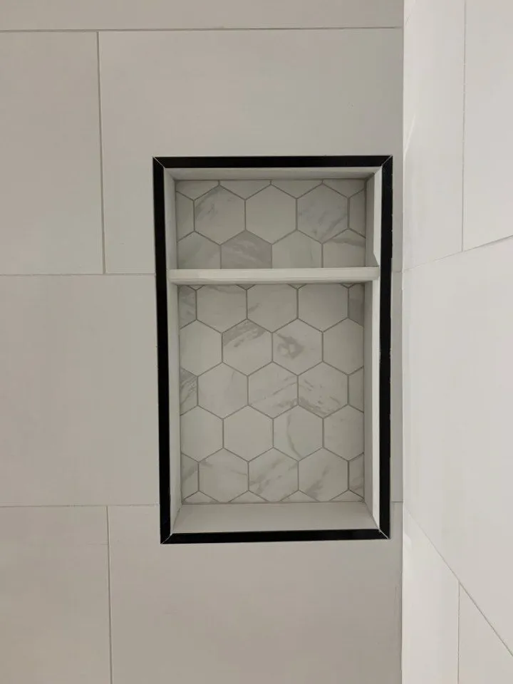 Vertical shower niche with matte black metal trim, marble hex mosaic interior, and shelf divider in a Tampa bathroom remodel by CMK