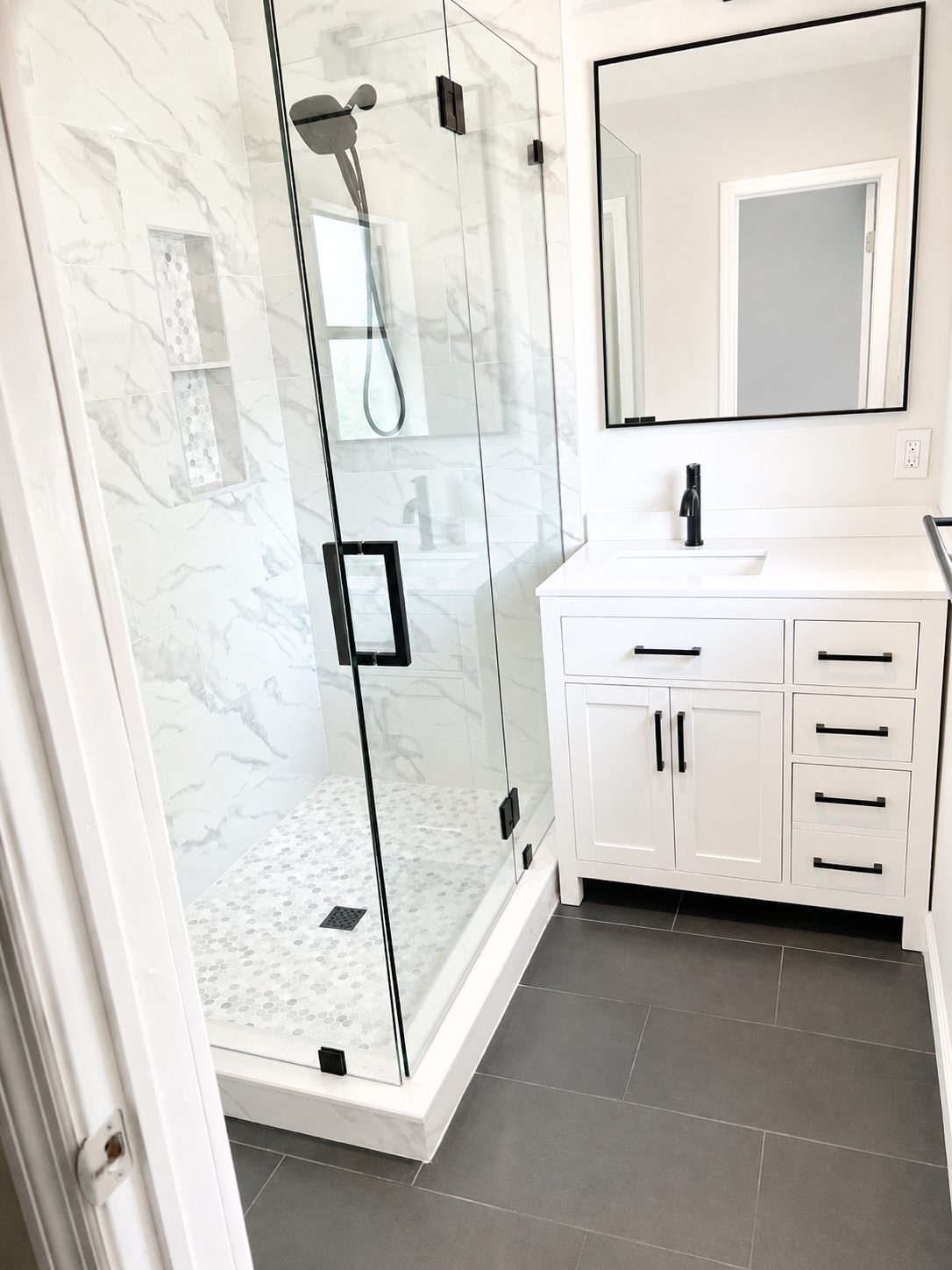 White shaker bathroom vanity with quartz countertop and matte black hardware beside a marble tile shower in Tampa