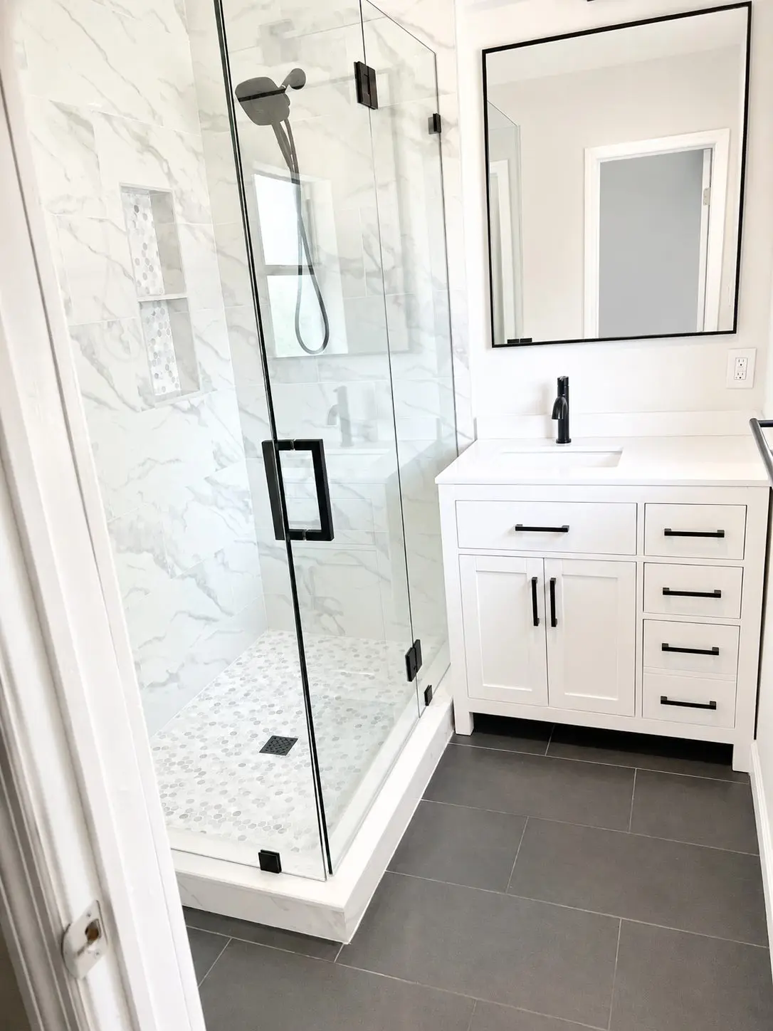 White shaker bathroom vanity with quartz countertop and matte black hardware beside a marble tile shower in Tampa