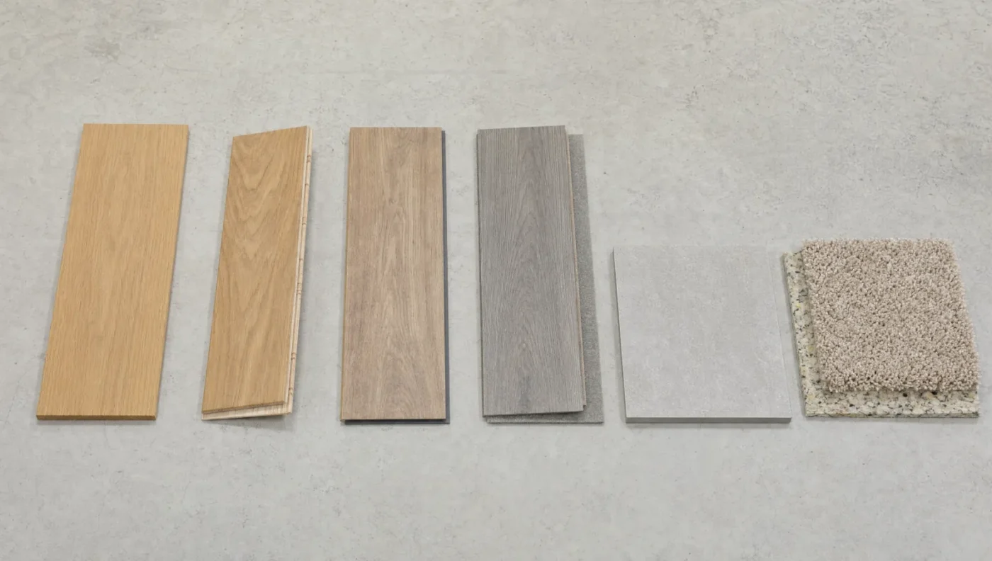 Six flooring samples side by side: solid oak, engineered wood showing its layers, laminate, rigid-core luxury vinyl plank, porcelain tile and carpet with padding