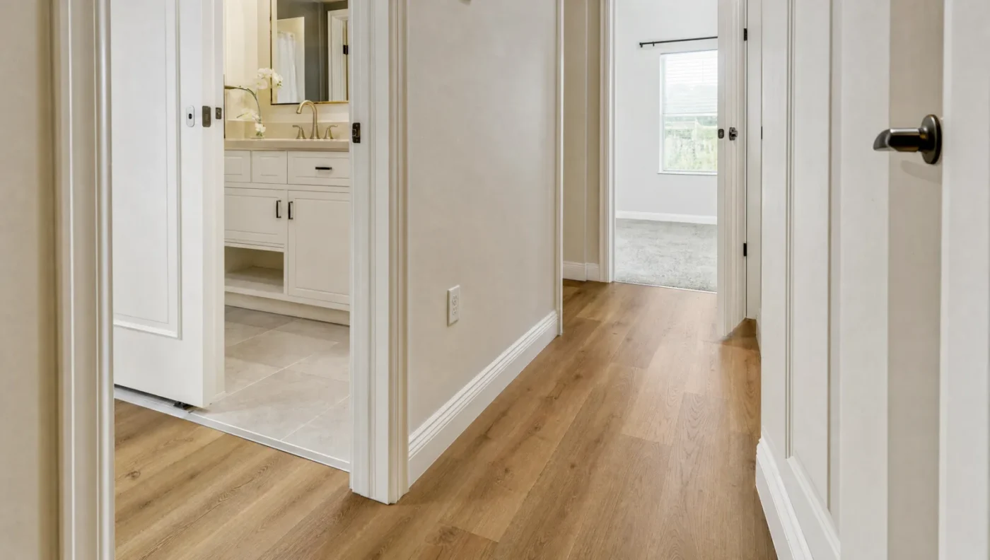 Hallway with wood-look luxury vinyl plank meeting porcelain tile at the bathroom doorway and carpet in the bedroom beyond